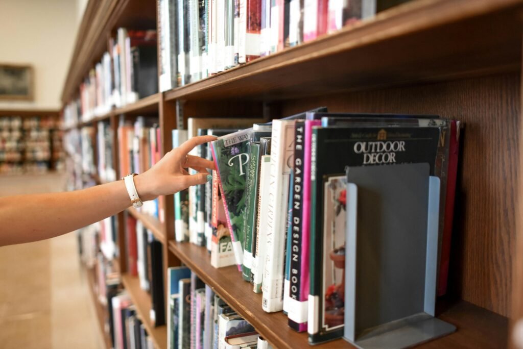 A close-up of a person's hand reaching for a book in a library shelf, suggesting exploration and learning.